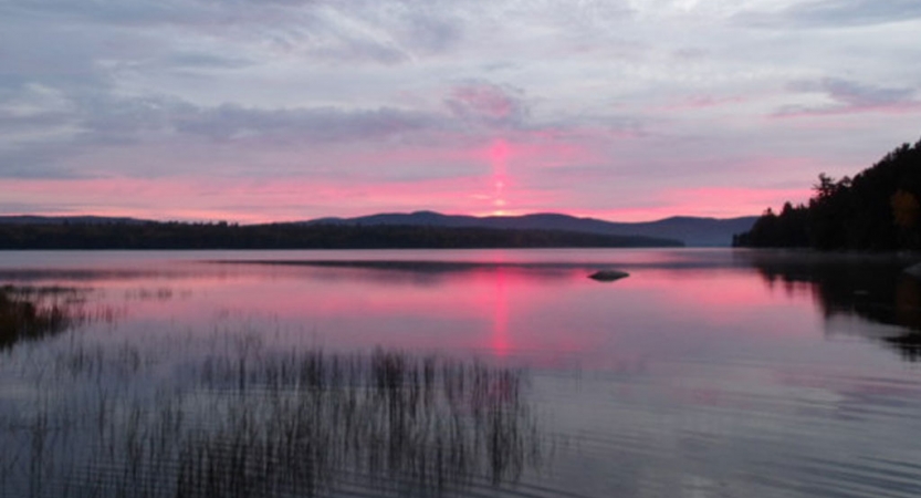 The sky appears in shades of purple and pink, and is reflected on a lake. 